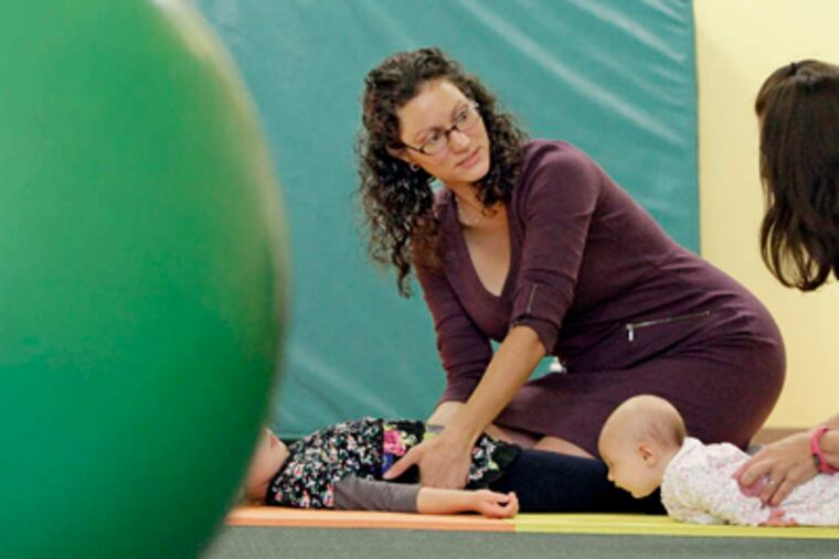 At her Grow Thru Play center, Tara Martello shows Jen McGown (right) how to perform calming tactile integration massage on 4-year-old Grace McGown, as 3-month-old Lydia McGown watches. Martello hopes to hire staff next year. ELIZABETH ROBERTSON / Staff