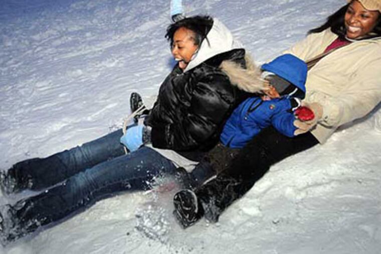 From left, Patrice Hundley, Isaiah Jenkins, 2, and his mother Chalice Jenkins sled down a hill at the corner of Dobbs Lane and Haddonfield-Berlin Road in Cherry Hill on Sunday. (Sarah J. Glover / Staff Photographer)