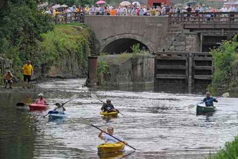 As a festive crowd watches, kayakers start down the Delaware Canal, riding the gentle surge of water released from the Lehigh River through the locks to the canal at Easton.