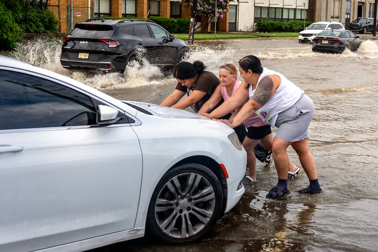 Husband Omar Marquez is behind the wheel as Angie Colon gets help from her mother and daughter pushing their car after it stalled while driving through high water on Ferry Avenue near PATCO station, the White Horse Pike and Route 130 in Camden Monday, July 6, 2026, as a flash flood threat continues for the region. The family was trying to get home nearby from shopping.