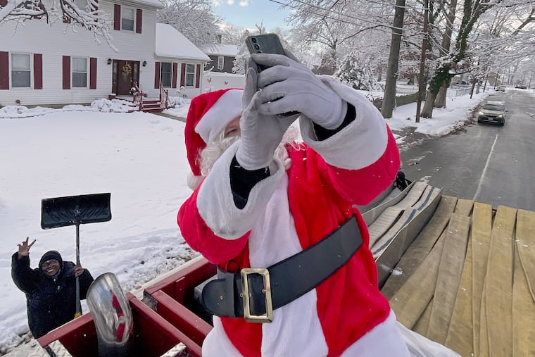 Jessica Johnson (left) poses with Santa after handing him her cell phone to take a selfie from atop his fire engine in the Barlow neighborhood in Cherry Hill Sunday, Dec. 14, 2025. The Cherry Hill firefighters with Engine 1352 were driving around delivering candy canes and Christmas spirit to children and residents.