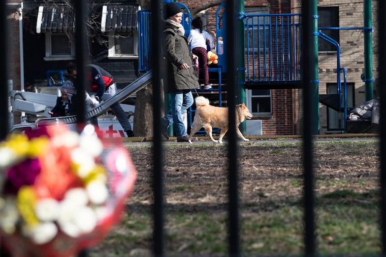 Metra LeBlanc walks her dog "Lea" pass a bouquet of flowers on a fence at the Gold Star Park in South Philadelphia. A South Philadelphia dog walker was killed in front of his fiancee in January 2019 after a dispute with another dog walker at Gold Star Park.