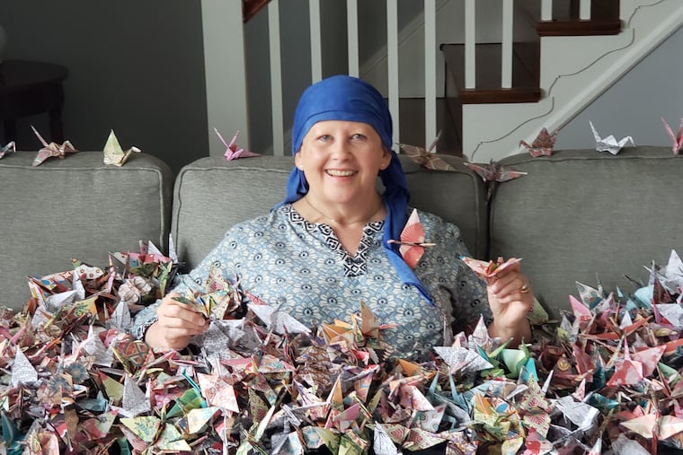 Beth Carlough, enveloped in the 1,000 origami cranes her friend Wendy Nowicki made to send her a message of love, support, and wishes for good health while Beth was undergoing cancer treatment. Between the pandemic and Beth's supressed immunity, Wendy could not hug her, but she could touch every one of these cranes.