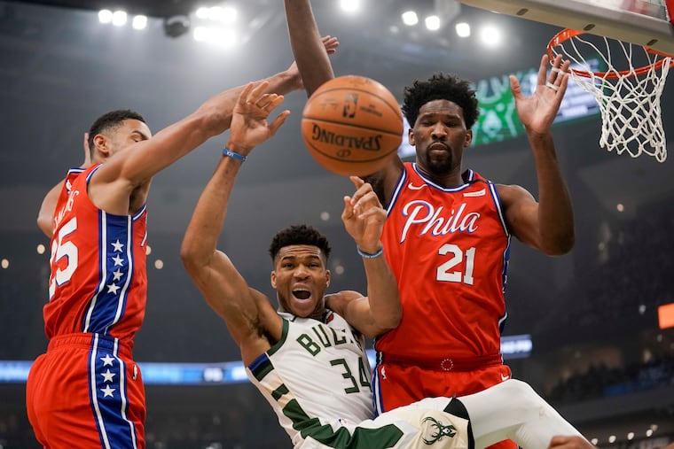 Milwaukee Bucks' Giannis Antetokounmpo is fouled as he drives between Philadelphia 76ers' Ben Simmons and Joel Embiid (21) during the first half of an NBA basketball game Saturday in Milwaukee.