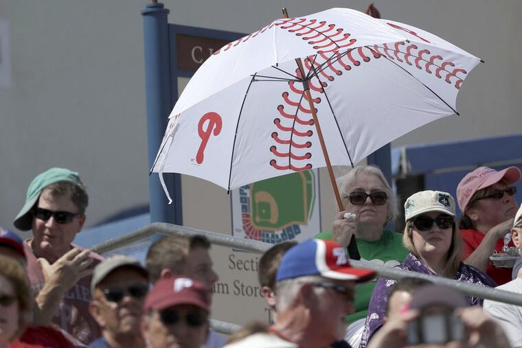 A fan covers herself with a umbrella as the Phillies play the Blue Jays in a spring training game in March in Clearwater.