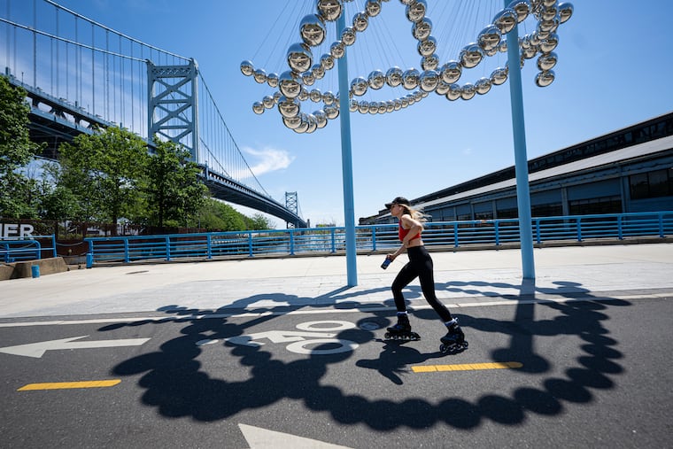 A person skates past the "Weaver's Knot: Sheet Bend" statue on Monday, May 12, 2025, along the Delaware River Waterfront, on a sunny spring day in Philadelphia.