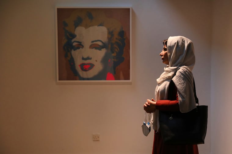 Fatemeh Rezaee, a retired teacher, stands next to Marilyn Monroe portrait by American artist Andy Warhol at Tehran Museum of Contemporary Art in Tehran, Iran, on Tuesday, Oct. 19, 2021. Iranians are flocking to Tehran's contemporary art museum to marvel at American pop artist Andy Warhol’s iconic work. Meanwhile in May, Christie’s will lead its marquee New York sales week with an auction of an Andy Warhol Marilyn silkscreen carrying an estimate in the region of $200 million. If the 1964 work, Shot Sage Blue Marilyn sells for that amount, it will be the most expensive 20th century painting to ever sell at auction, according to Christie's.(AP Photo/Vahid Salemi)
