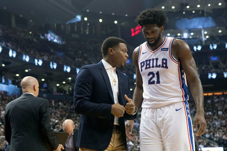 Joel Embiid (21) talks to injured Raptor Kyle Lowry after his scoreless outing.