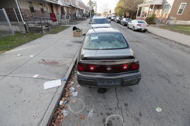 Circles on the 5500 block of Pearl Street in West Philadelphia indicate where shell casings were found after a shooting Sunday that wounded a 14-year-old and left a 23-year-old man dead. Police later towed the Chevrolet Impala pictured here as evidence.