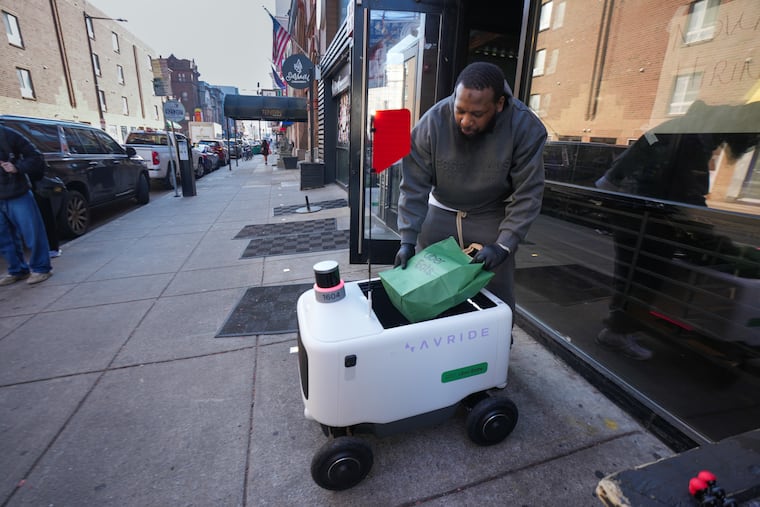 Lavelle "Garci" Peterkin, owner of Carter's Cheesesteaks by Garci in Chinatown, demonstrates the loading of an Uber Eats robot.