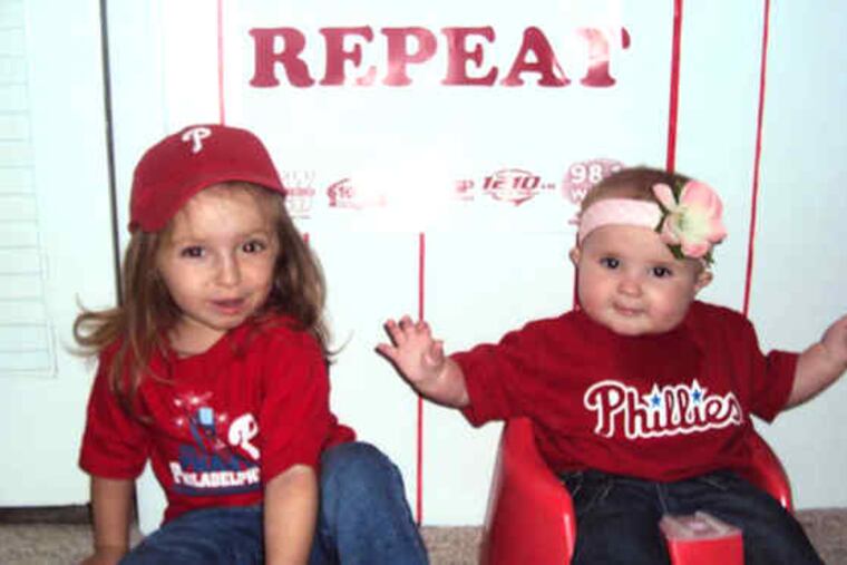 Grace Walsh (left), 2, and sis Finnley, 7 months, discussed their hopes for a Phillies win in their Havertown basement recently. Both agreed they did not want to wait another 28 years for a championship. Parents Jen and Dan Walsh, lifelong Phillies phanatics, agree.