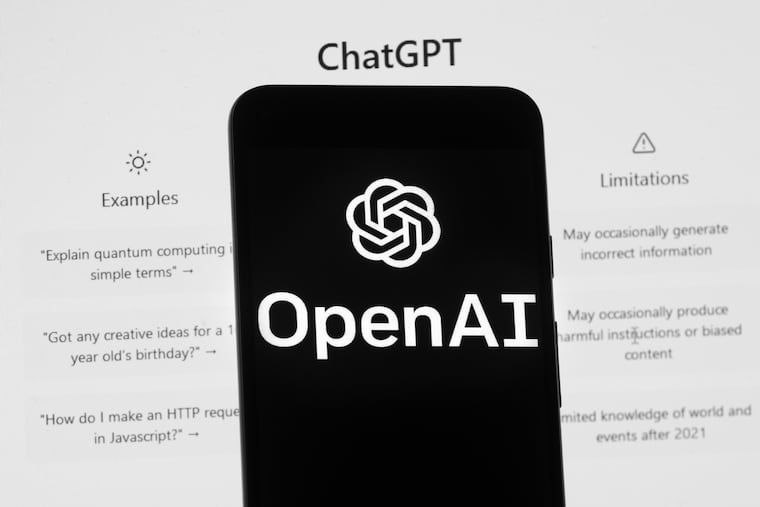 The OpenAI logo is seen on a mobile phone in front of a computer screen which displays the ChatGPT home Screen, on March 17, 2023.