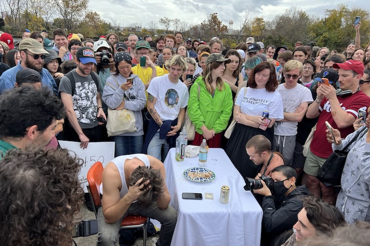 Alexander Tominsky, a.k.a. the Chicken Man, holds his head in his hands in front of a crowd of onlookers as he attempts to finish his 40th rotisserie chicken in 40 days on an abandoned pier in South Philly on Nov. 6, 2022.