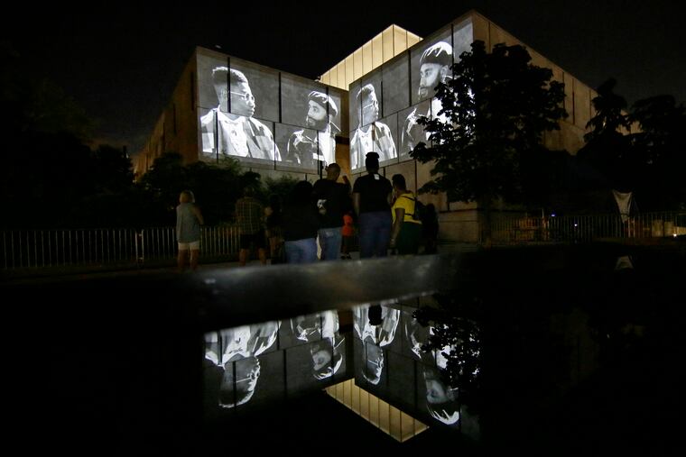 People watch From the Root to the Fruit: Portraits of Black Fathers and Their Children being projected onto the exterior of the Barnes Museum on Saturday night.