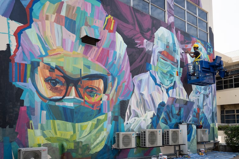 A worker gave final touches to a graffiti that tributes to Malaysian workers on the frontline against the COVID-19 pandemic outside a hospital in Kuala Lumpur, Malaysia, Friday, Jan. 29, 2021. The pandemic has produced many surprises. (AP Photo/Vincent Thian)