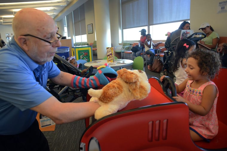 Volunteer and Penn Memory Center patient Leslie Wolff entertains Alli-Jo Tupper (right) with his puppets at CHOP Care Network.