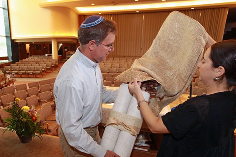 Rabbi Adam Zeff, left, of the Germantown Jewish Centre, holds the torah scroll as Assistant Rabbi Annie Lewis, right, covers the scroll in white for the upcoming high holiday of Yom Kippur. ( MICHAEL BRYANT / Staff Photographer )