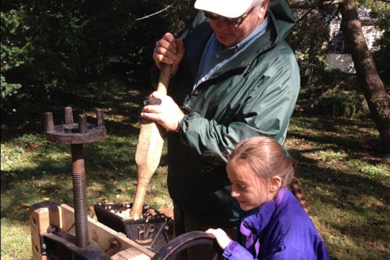 Scott Blunk, a retired farmer who now volunteers at Weavers Way, shows Gretta Maguire, 8, how to make all-natural apple juice in an old-fashioned press. "Why don't we volunteer?" Gretta asked her father. Photo Julie Zauzmer