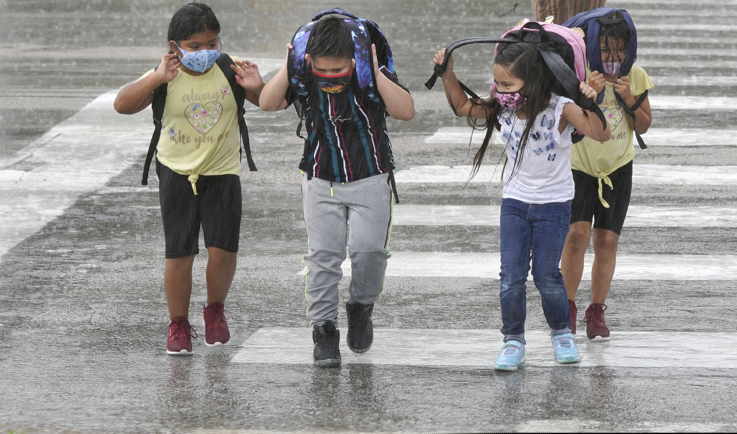 Elementary school children wear masks as they make their way across the street after school let out during a rain storm in Richardson, Texas.