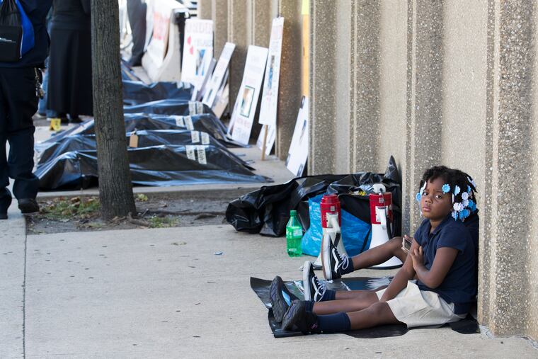 Plastic bags were used to represent body bags at the 2nd day of silent protests held by the families of unsolved murder victims by Police Headquarters. Kaliah, front, and Maliyah Alford sit on the sidewalk on Sept. 25, 2019. Their father, Zakiyy Alford was murdered June 19, 2017 and is still an unsolved murder.