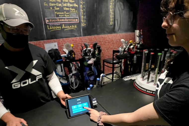 X-Golf manager J.W. Park (left) helps Ashley Moreno to check out at X-Golf indoor golf in Glenview, Ill., in early January.