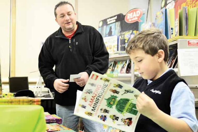 Bob Markart, the parent of a first grade son and third grade daughter at Our Lady of Assumption School in Atco, volunteers at a book sale in the school library, helping second grader Matthew DeStefano (right) purchase some books January 28, 2013. The diocese says the school has to raise more than $150,000 to remain open next year. The parents and grandparents are fundraising like crazy. ( TOM GRALISH / Staff Photographer )