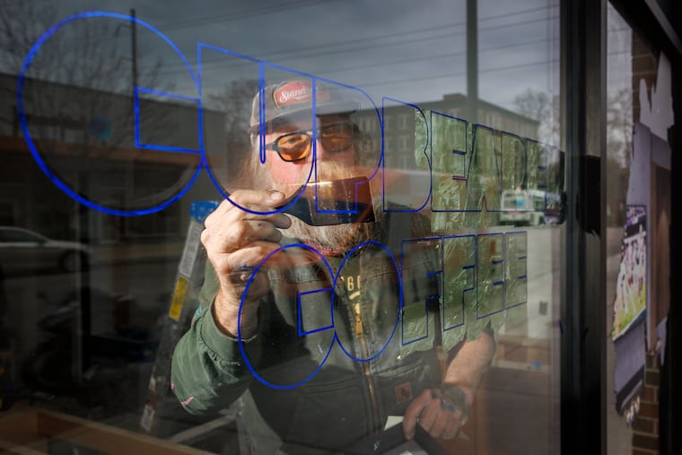 Gibbs Connors working on a sign for Cupbearer Coffee on the 300 block of West Chelten Avenue in Philadelphia. He is applying gold leaf to the letters on the front window.