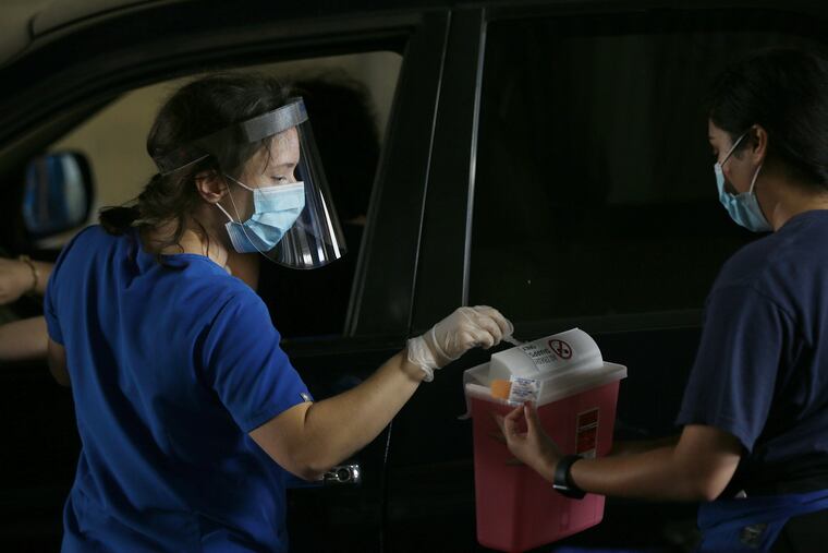 Volunteer Luise Weber (left), a nurse, puts a syringe into a sharps disposal container held by fellow volunteer Chandni Patel after administering a flu shot during a drive-through clinic for police officers and their family members at the Delaware Valley Intelligence Center in South Philadelphia on Oct. 21, 2020. The clinic was organized this year by the city health department and Law Enforcement Health Benefits.