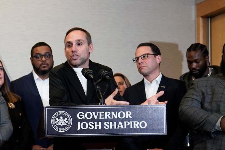 Gov. Josh Shapiro (right) looks on as Philadelphia 76ers co-owner Michael Rubin speaks at a lectern during a 2023 ceremonial bill signing in Philadelphia. Shapiro’s acceptance of in-kind contributions from Rubin has raised questions from good government advocates.