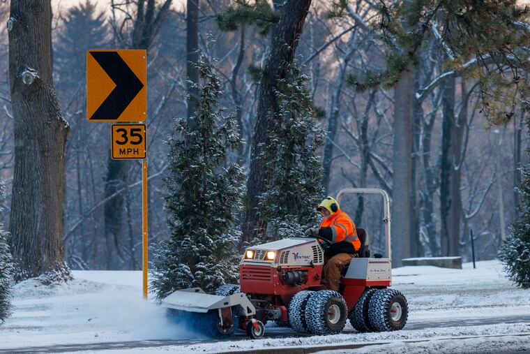 A maintenance worker clears snow along a sidewalk beside the Walnut Lane Golf Club in Philly Friday. In all likelihood, more snow will fall on Sunday in that part of the city.