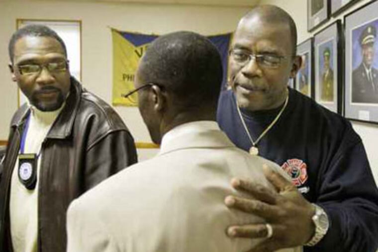 Firefighter Kenneth Greene Sr. (far right) hugs Lewis Harris Jr (middle) as Roberty Kirby (left) looks on after a press conference announcing a lawsuit against Local 22 of firefighters union. ( Elizabeth Robertson / Staff Photographer )