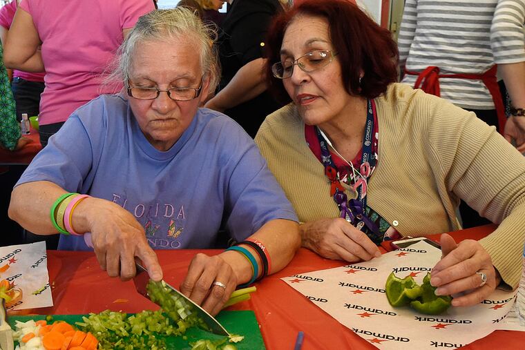 Carmen Figueroa practices her slicing skills after the chefs’ demonstration, as her friend Carmen Laureano watches. One participant says the classes have made her more aware of what she buys at the grocery, including, for the first time, kale.