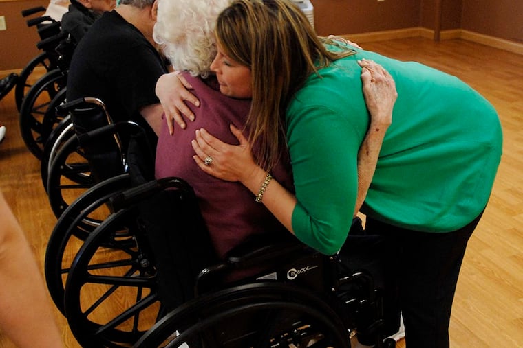 Staff member Stacy Omar hugs a resident during a memorial service at the center. An administrator said residents were asking for more opportunities to express their wishes, now that they know staff is listening. ( Bradley C Bower / For the Inquirer )
