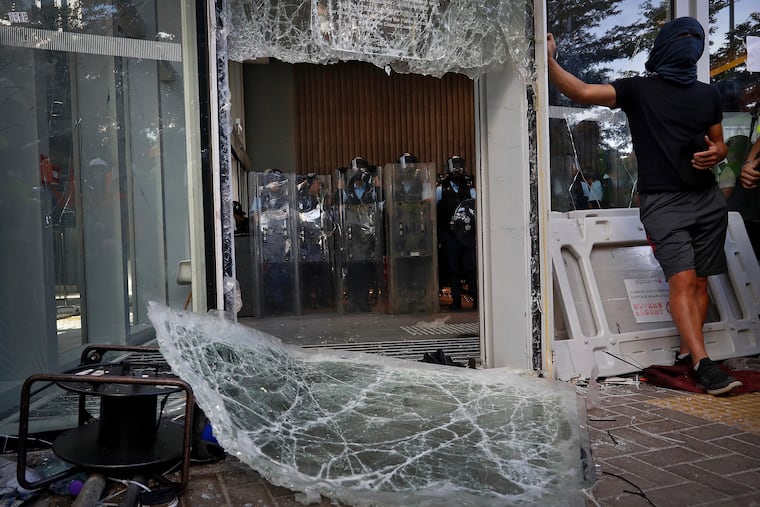 Police officers with shields stand guard behind the damaged glass of the Legislative Council in Hong Kong after protesters tried to break in.