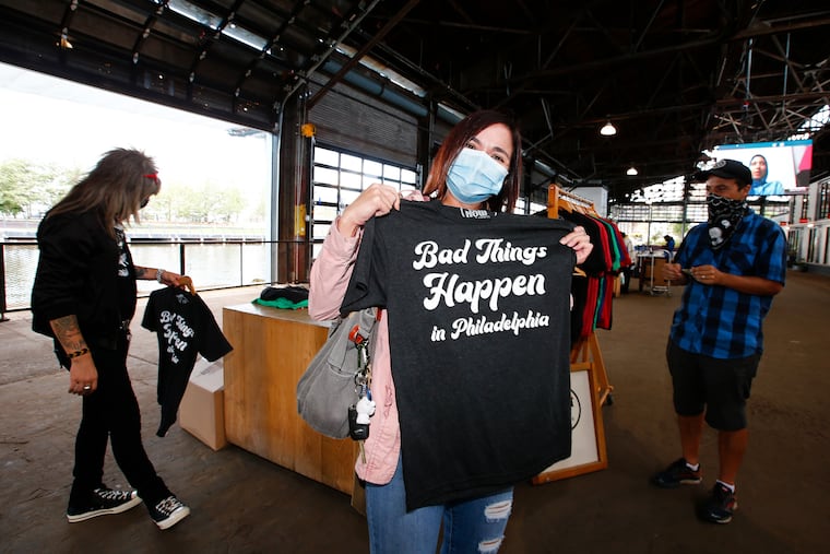 Customer Nadine Michael holds-up her Bad Things Happen in Philadelphia t-shirt as Do It Now T-Shirts owners Johnny Douglas (left) and Matt Charles prepare to sale their designed t-shirts at the Cherry St. Pier Fall Artist and Artisans Market on Friday, Oct 2, 2020.