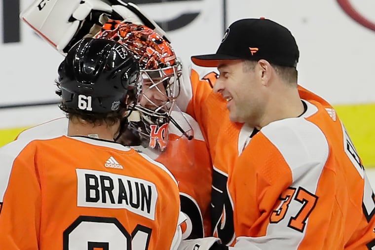 Flyers goalie Carter Hart is greeted Wednesday by teammates Brian Elliott (right) and Justin Braun after he blanked New Jersey, 4-0, for his first career shutout. Hart, 21, became the youngest player in Flyers history to register a shutout.