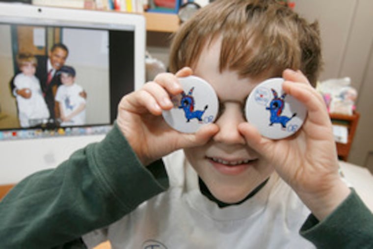 Simon Shankweiler, 8, with a photo of himself, his brother Henry and Barack Obama on the computer screen at his Swarthmore home, models buttons of the famous donkey he did for the campaign.