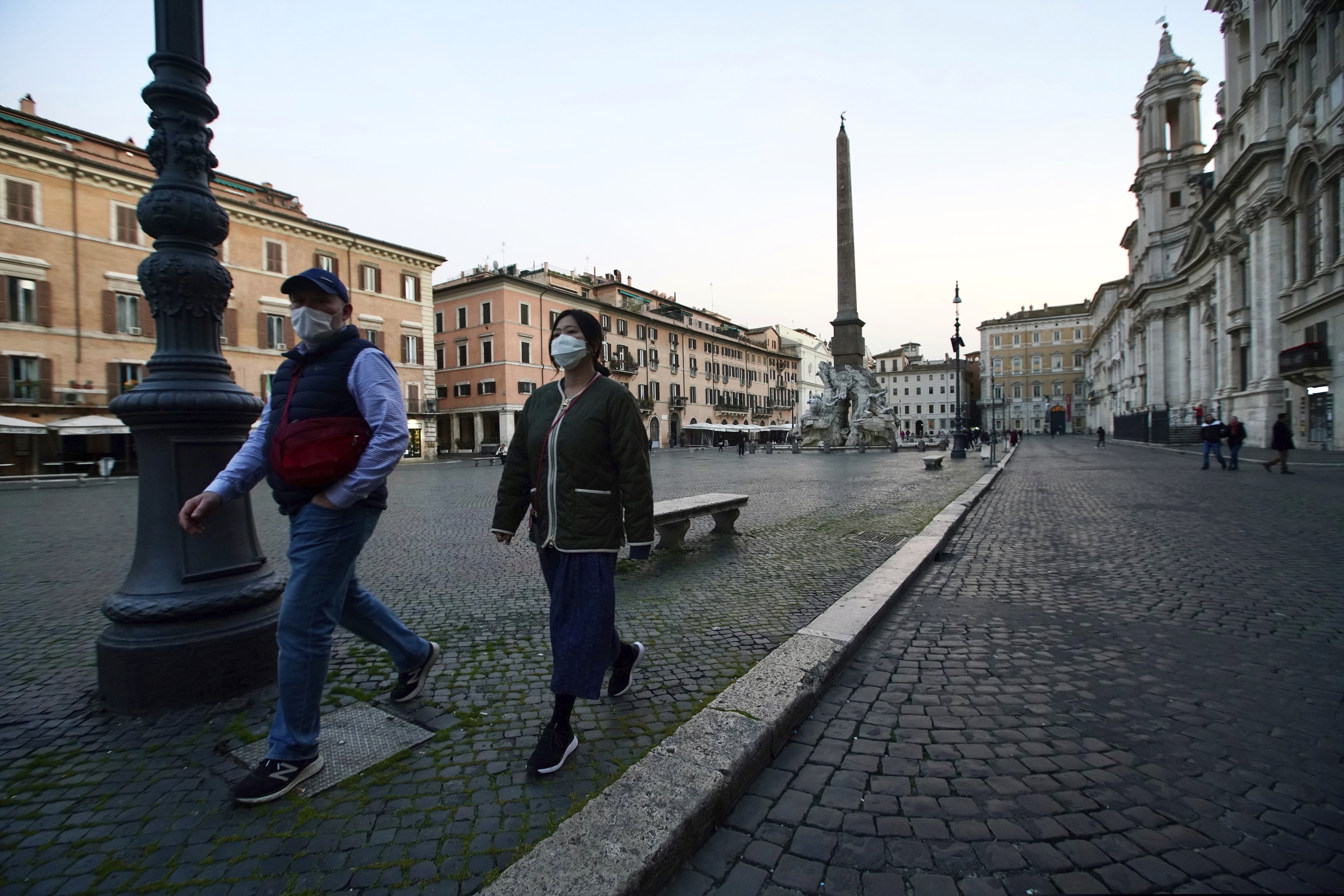 Two people walk in Rome's Piazza Navona, deserted, on March 10, 2020. For most people, the new coronavirus causes only mild or moderate symptoms, such as fever and cough. For some, especially older adults and people with existing health problems, it can cause more severe illness, including pneumonia. (AP Photo/Andrew Medichini)