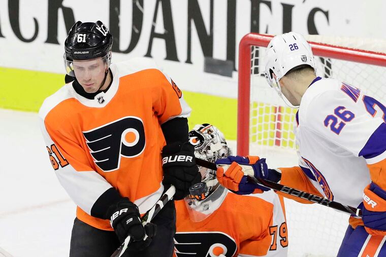 Flyers defenseman Justin Braun blocks the puck with his glove in front of goaltender Carter Hart against the New York Islanders' Oliver Wahlstrom on Jan. 30. The Flyers won in overtime, 3-2. Hart will face the Isles on Saturday.