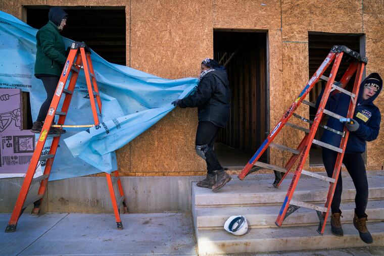 Cathy Brzozowski (left) and her daughter Morgan Brzozowski (right) volunteer with Talini Mathis (center), a Habitat for Humanity AmeriCorps member, to put house wrap around a set of rowhouses in 2020.