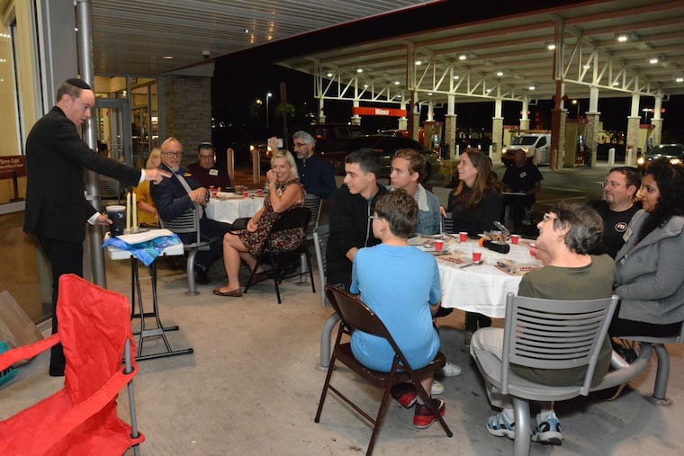 Performance Artist Brian Feldman (left, standing), tells guests at Wawa Shabbawa, a Friday night dinner that celebrates the Jewish Sabbath at a Wawa convenience store, to raise their cups of grape juice for the Kiddush, a blessing over what is typically wine.