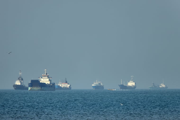 Cargo ships, including bulk carriers and general cargo vessels, sit at anchor offshore as a small motorboat passes in the foreground, in the Strait of Hormuz off Bandar Abbas, Iran, Monday, May 4 , 2026.