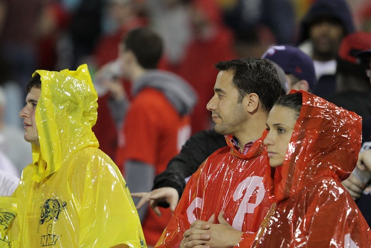 Fans watch as the ground crews cover the field during a rain delay during an early-season game. Rain is a threat on Monday as the Phils attempt to play their home opener.