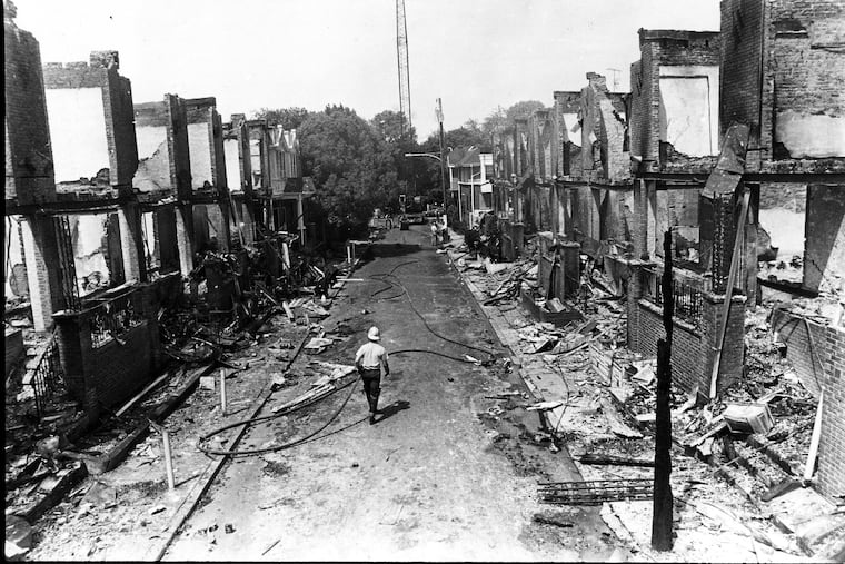 A Philadelphia firefighter walks down a burned-out Osage Avenue days after the confrontation with MOVE in May 1985. Progress addressing racism, poverty, and police brutality has been too slow and too little for too many, the Editorial Board writes.