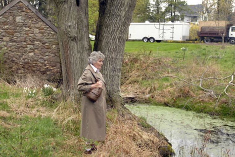 Christine Fisher stands near a springhouse and pond on property near Skippack Pike where groundwater was contaminated because of a leak from a gas station. “After a rain, we find these little puddles of sheen back in the woods here, still,” she said. (Ron Tarver / Staff Photographer)