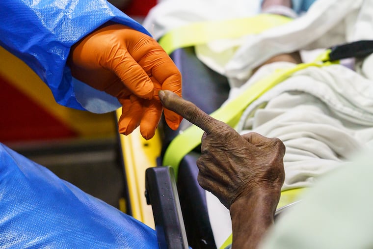 Narberth ambulance paramedic Tim Mumford,holds the finger of a patient while treating the patient, in the ambulance outside Rosemont Care & Rehabilitation Center in Bryn Mawr. The patient had symptoms consistent with Covid-19. Pennsylvania officials on Tuesday released plans to test every resident and staff member at the state's hundreds of nursing homes and long-term care facilities.