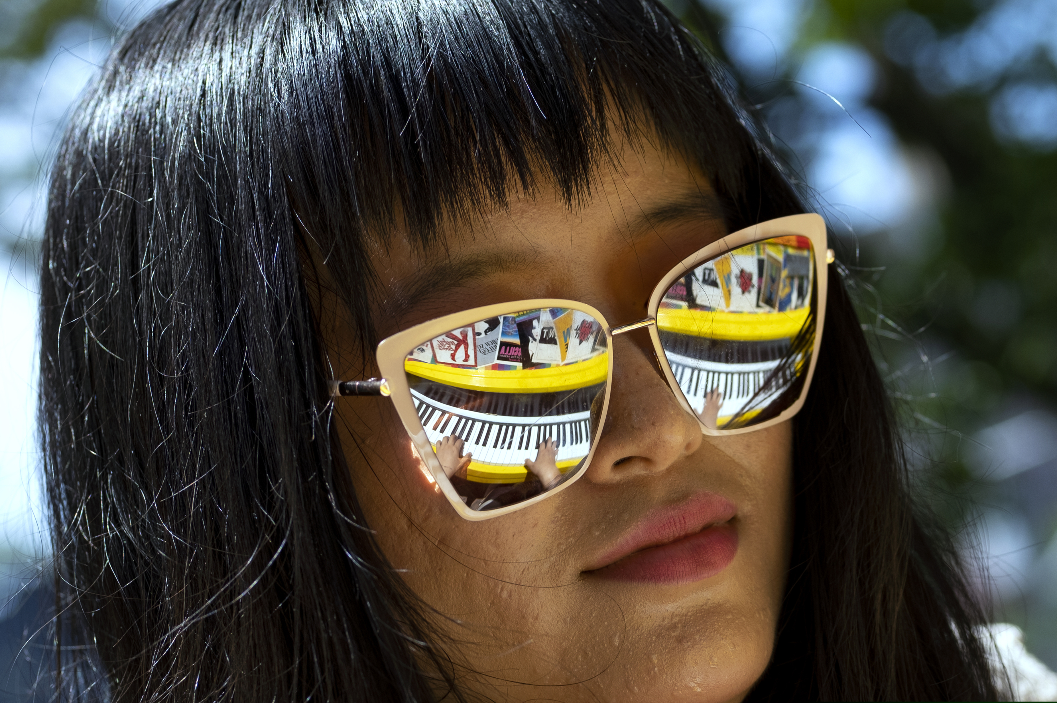 Holly Yiping Wang of New York plays a piano adorned with Broadway Playbills (reflected in her sunglasses) at the Stonewall National Monument, near the Stonewall Inn, Saturday, June 29, 2019, as she and others take part in activities and events marking the 50th anniversary of the Stonewall uprising in New York. (AP Photo/Craig Ruttle)