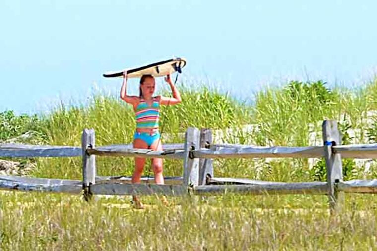 Twelve year old Brittany Jones of Glenmore carries her surfboard across the wide dunes in Avalon, on the beach at 14th Street August 2, 2013. Earlier in the week, visiting Dutch levee and dike engineers visited Avalon to exchange their ideas about water with New Jersey Shore officials in a new partnership. ( TOM GRALISH / Staff Photographer )