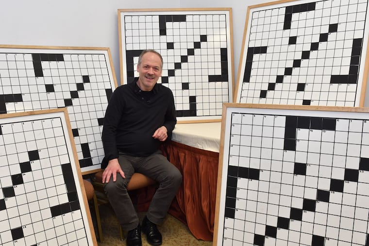 Will Shortz, founder and director of the American Crossword Puzzle Tournament, sits amid large crossword puzzle whiteboards used in the tournament's championship rounds.