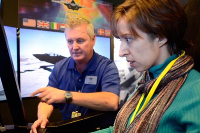 Gina Diorio (right) district director for US Congressman Scott Garrett, gets help from Tony Stutts, test director for the F-35 simulator as she tries out the training device during a press event on the U.S. military's latest fighter at Lockheed Martin Mission Systems & Sensors Satellite Facility in Moorestown November 3, 2011. ( TOM GRALISH / Staff Photographer )